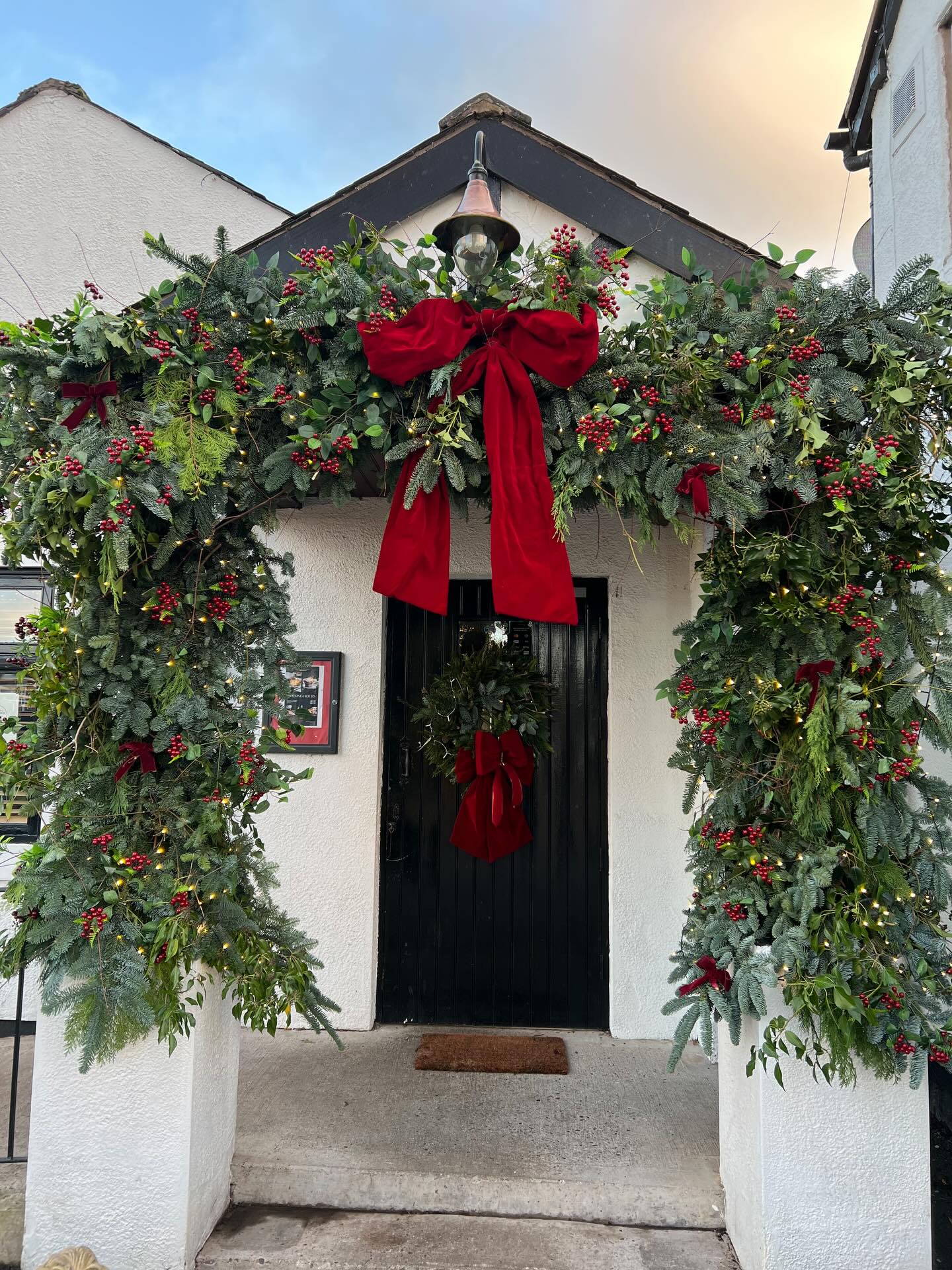 Large Christmas greenery arch with red bows framing an entrance