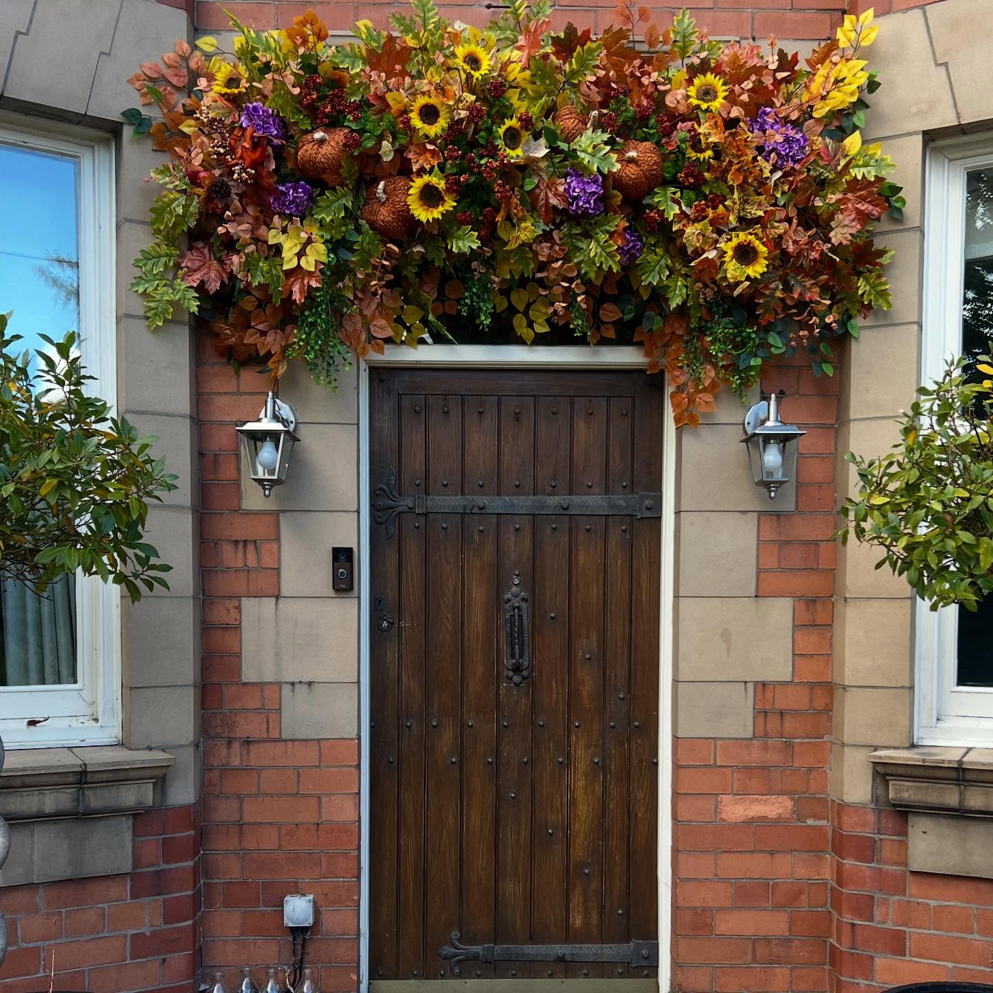 Autumn flowers, foliage and pumpkins surrounding a dark wooden front door
