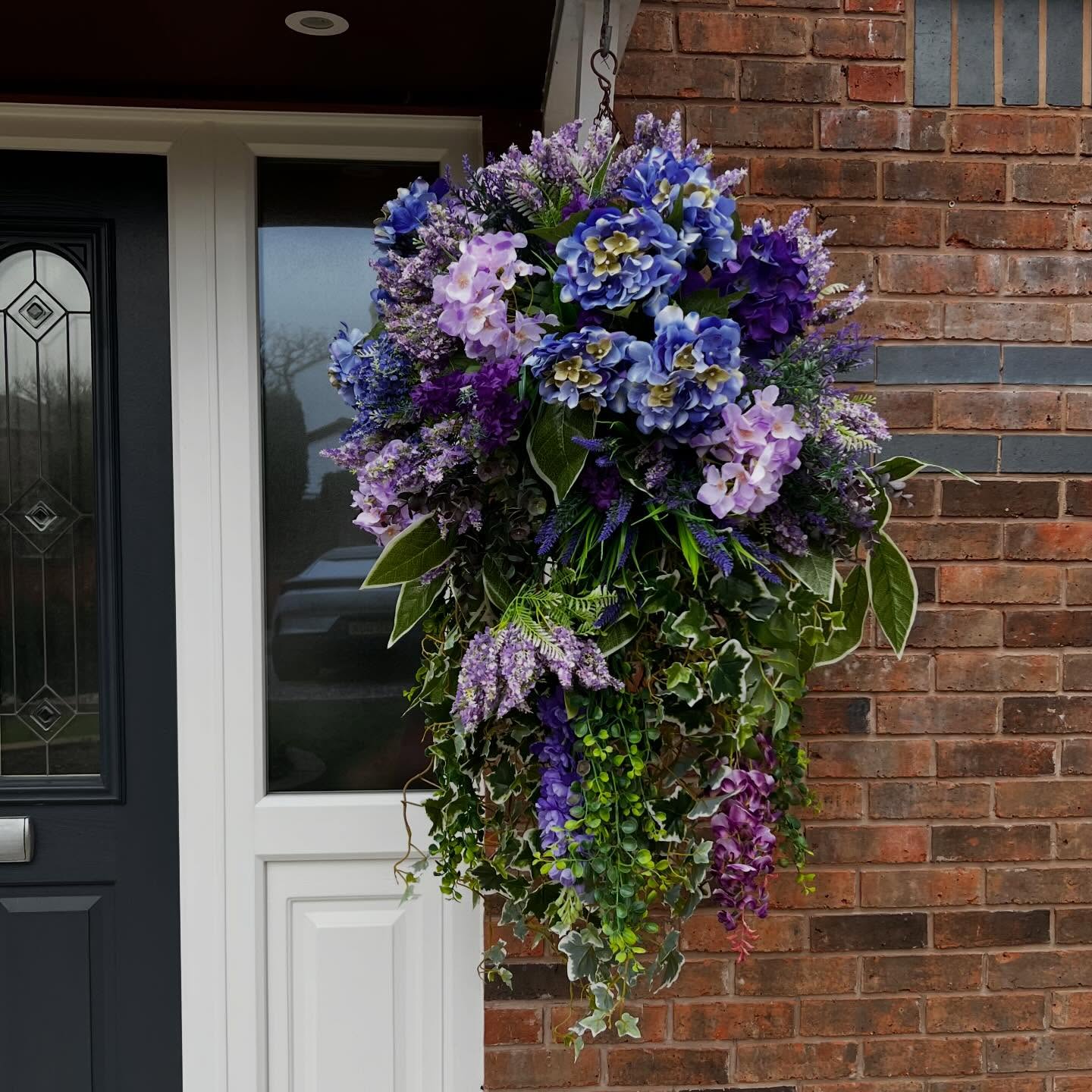 Abundant purple and green floral wreath on a dark front door